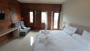 A bedroom with a large bed, a wooden bench, a TV mounted on the wall, and a window with curtains. - Saghara Villa Amed (Karangasem)