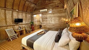 A rustic wooden room with a bed, a television, a table, and chairs. - The Suwi Huts (Penida Island)