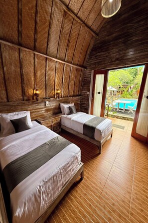 A room with two beds, wooden walls, and a view of an outdoor swimming pool. - The Suwi Huts (Penida Island)