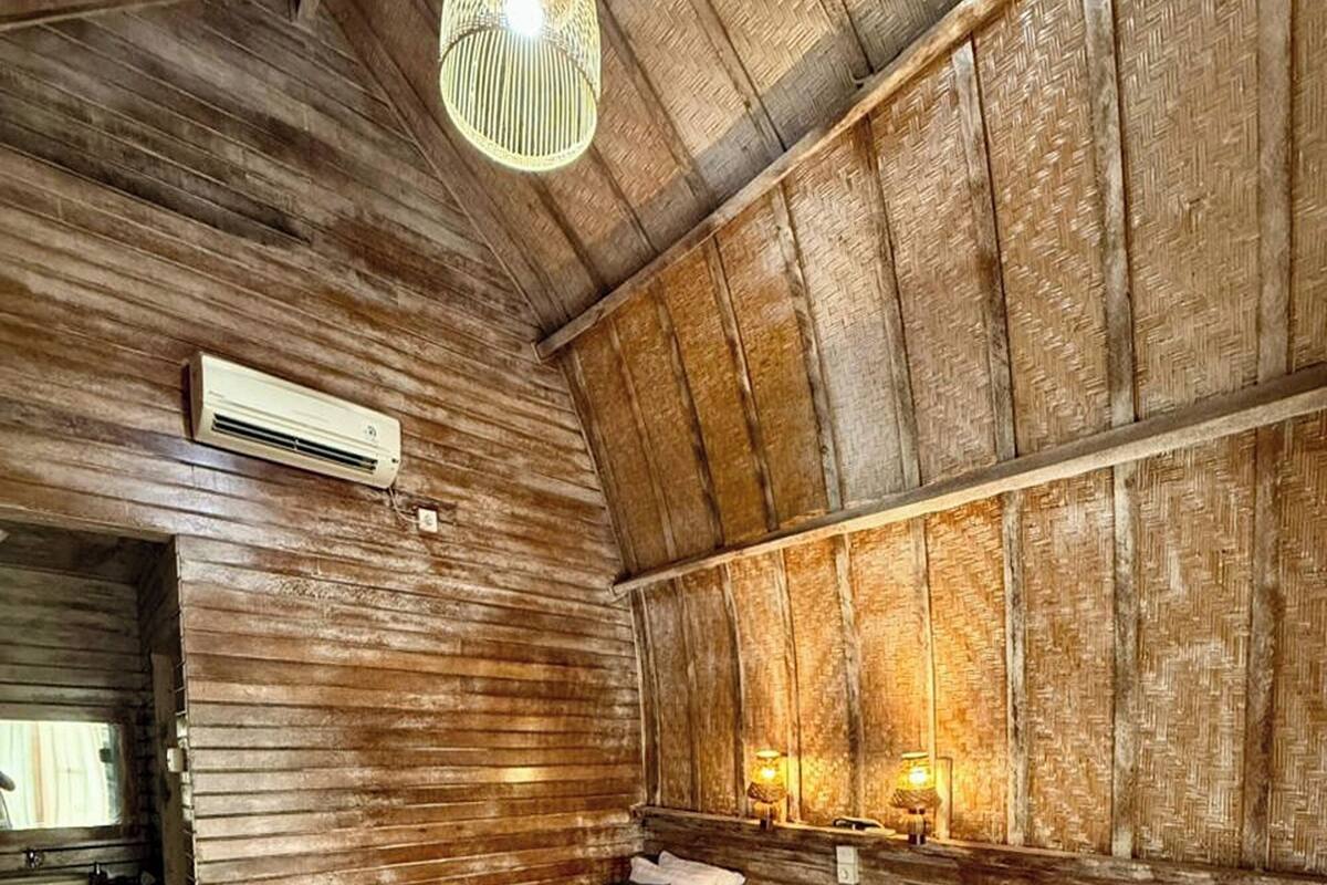 A rustic wooden room with two beds, a hanging light fixture, and a visible air conditioning unit.