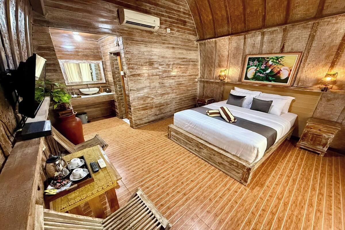 A wooden-themed bedroom with a bed, bedside table, and a painting on the wall.
