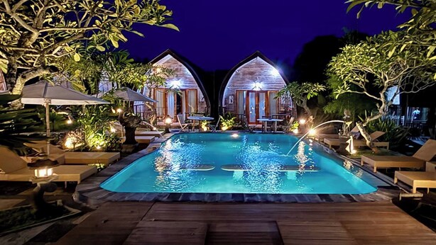 A swimming pool surrounded by wooden deck and lounge chairs, with two wooden cabins in the background. - The Suwi Huts (Penida Island)