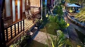 A wooden villa with a covered porch, a small pool, and lush tropical landscaping. - The Suwi Huts (Penida Island)