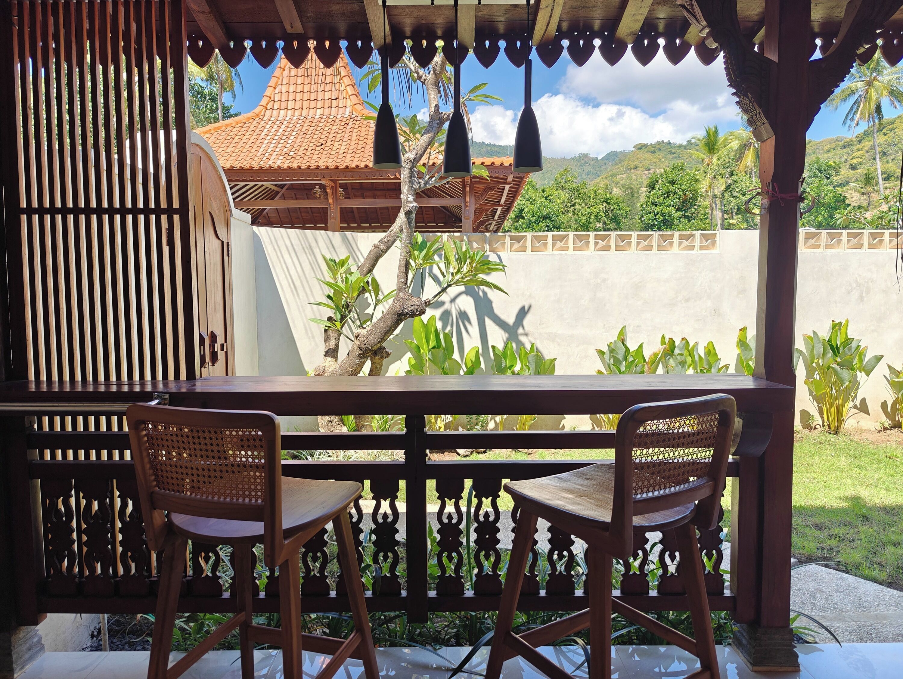 Une table en bois avec deux chaises, une clôture décorative en bois et une vue sur un bâtiment doté d’un toit en tuiles.