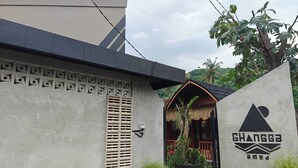 A modern building with a geometric facade, a thatched-roof structure, and a prominent logo. - Ghangga Amed (Karangasem)