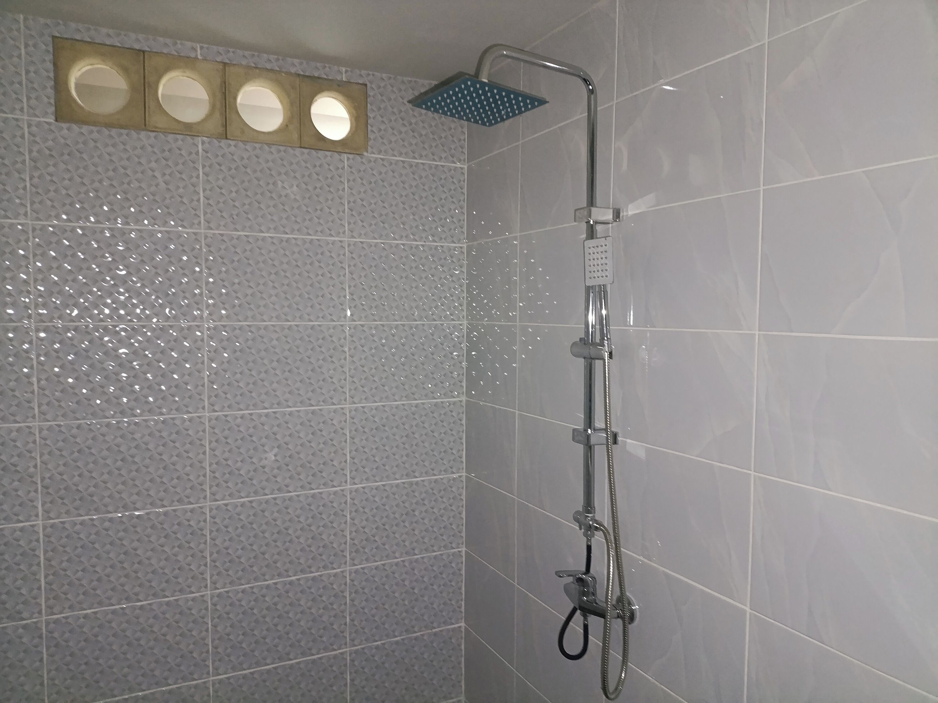 Ducha con cabezal de ducha de mano y panel de control en la pared.
