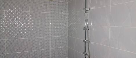 Ducha con cabezal de ducha de mano y panel de control en la pared.