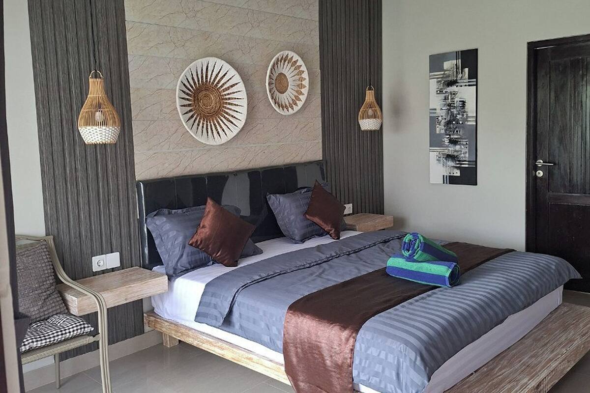 Une chambre à coucher moderne avec un grand lit, une table de chevet, une chaise et des œuvres d’art décoratives au mur.