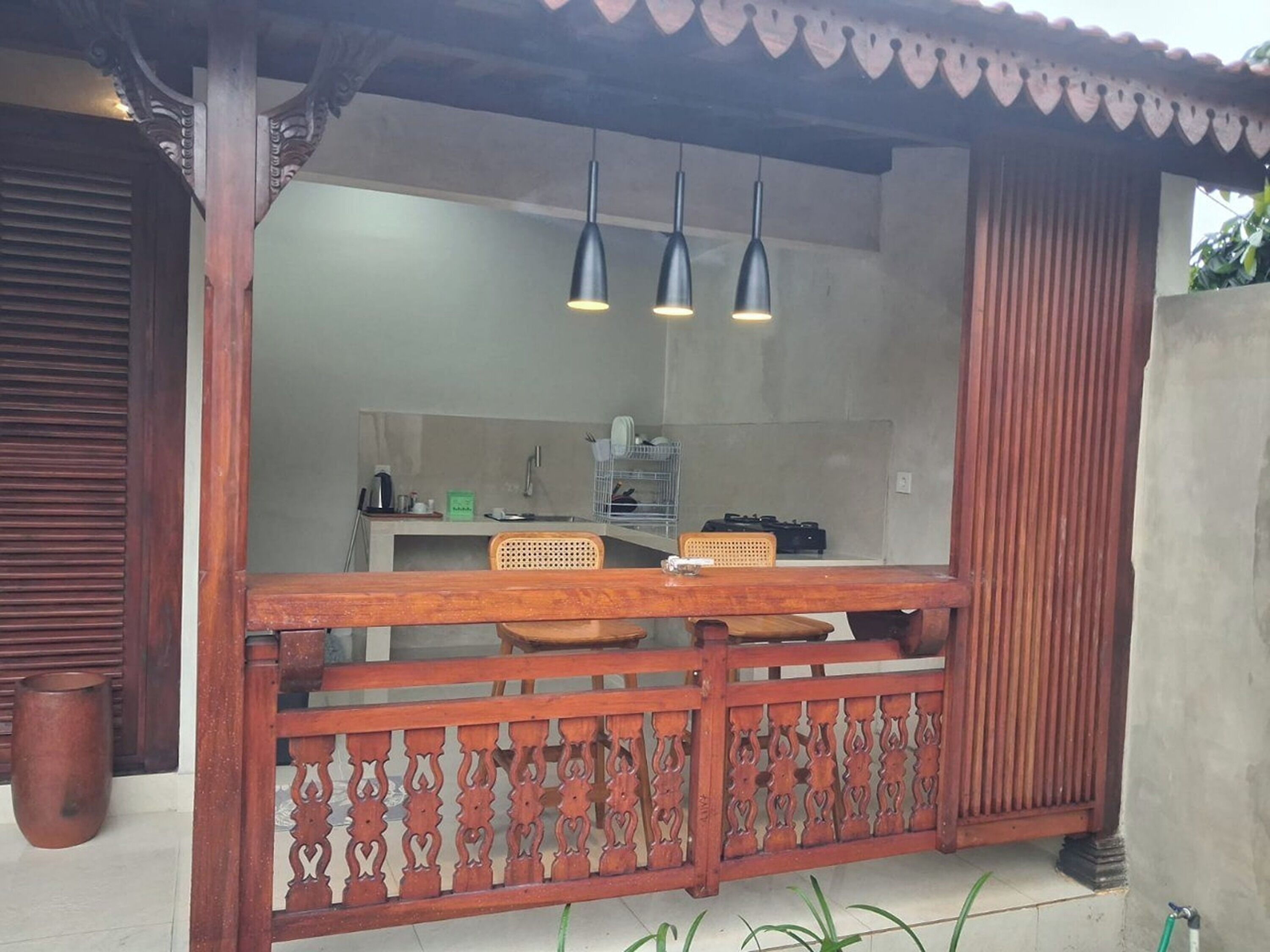 A wooden outdoor kitchen with a built-in counter, hanging pendant lights, and a decorative fence.