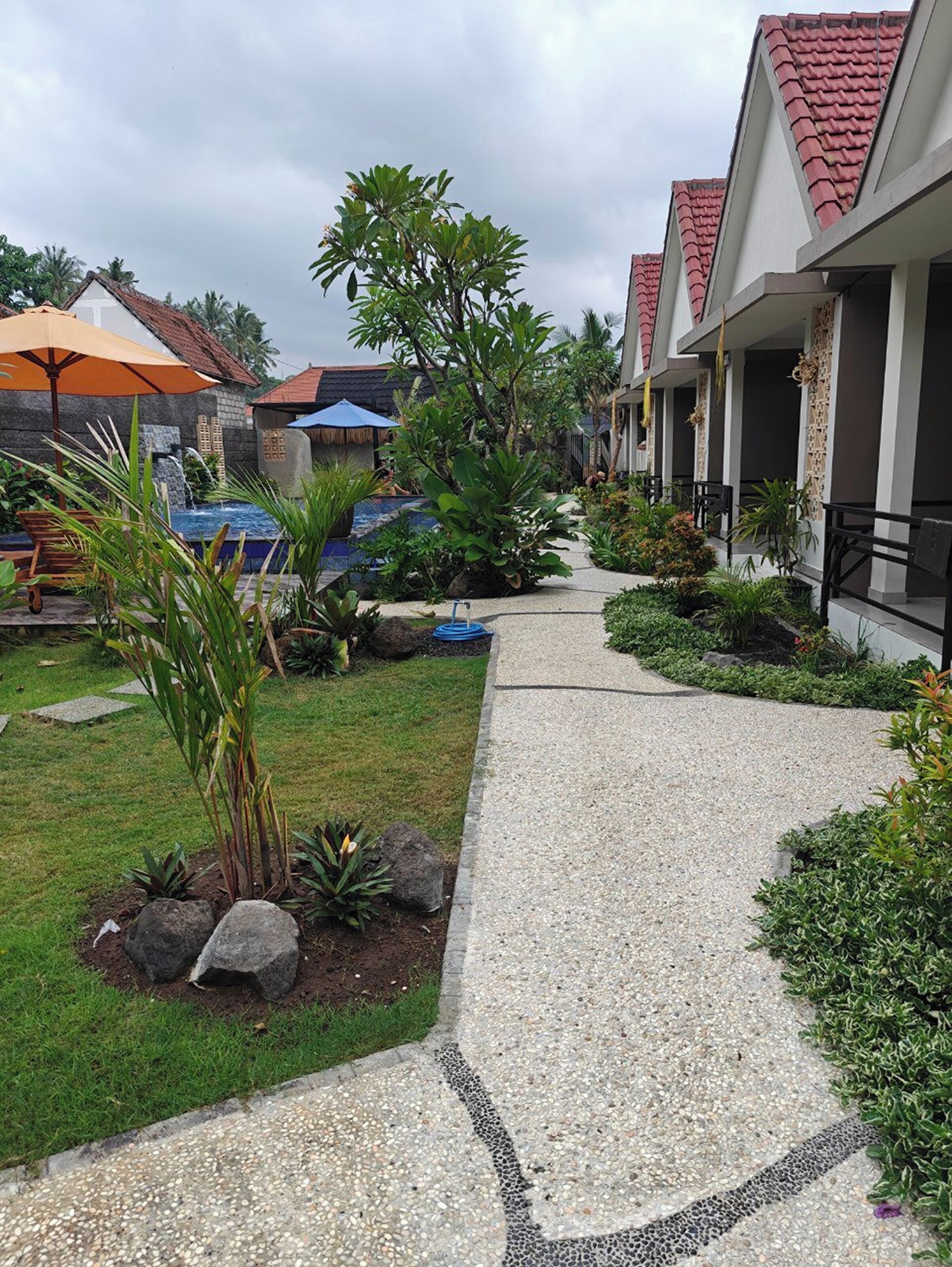 A pathway leading to a building with a tiled roof, surrounded by lush greenery and a small water feature.