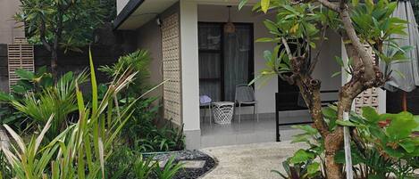A modern house with a sloped roof, a front porch with chairs, and a garden with various plants.