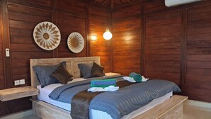 A wooden-paneled bedroom with a bed, pillows, a bedside table, and wall decorations. - Ghangga Amed (Karangasem)
