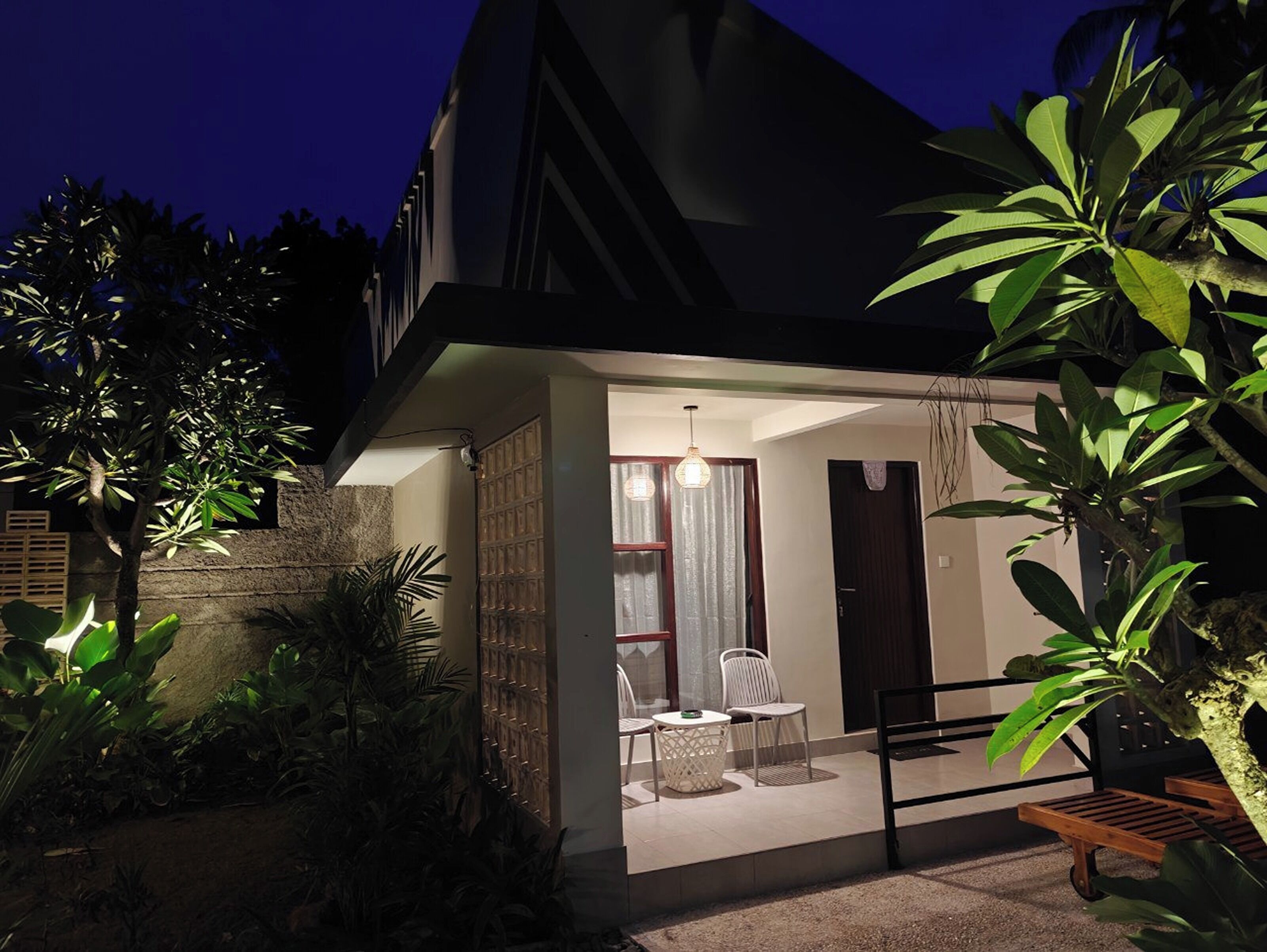 A modern house with a patio area featuring a table and chairs, surrounded by lush greenery.