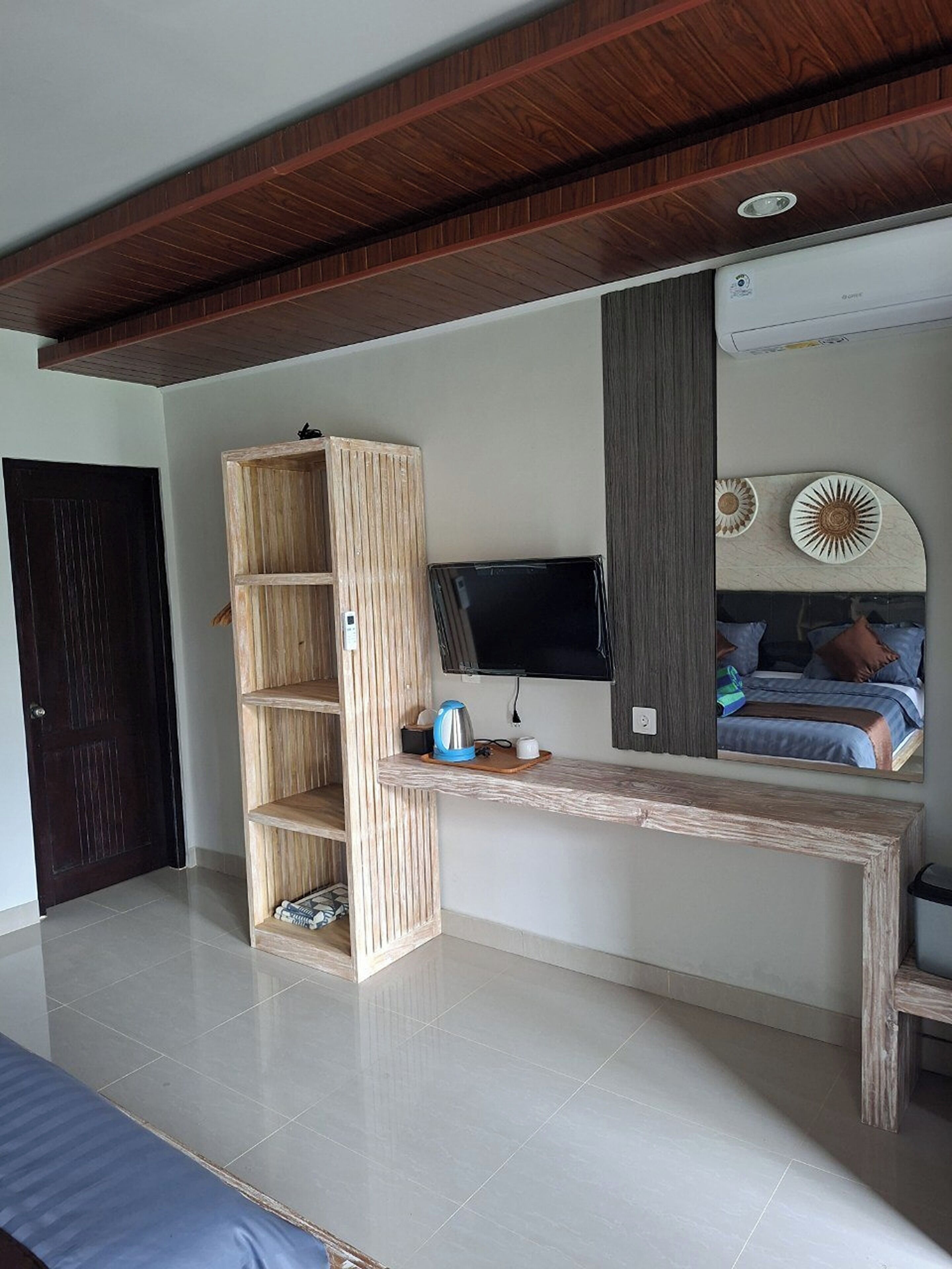 A bedroom with a wooden bookshelf, a flat-screen TV, a bed, and a mirror reflecting the room.