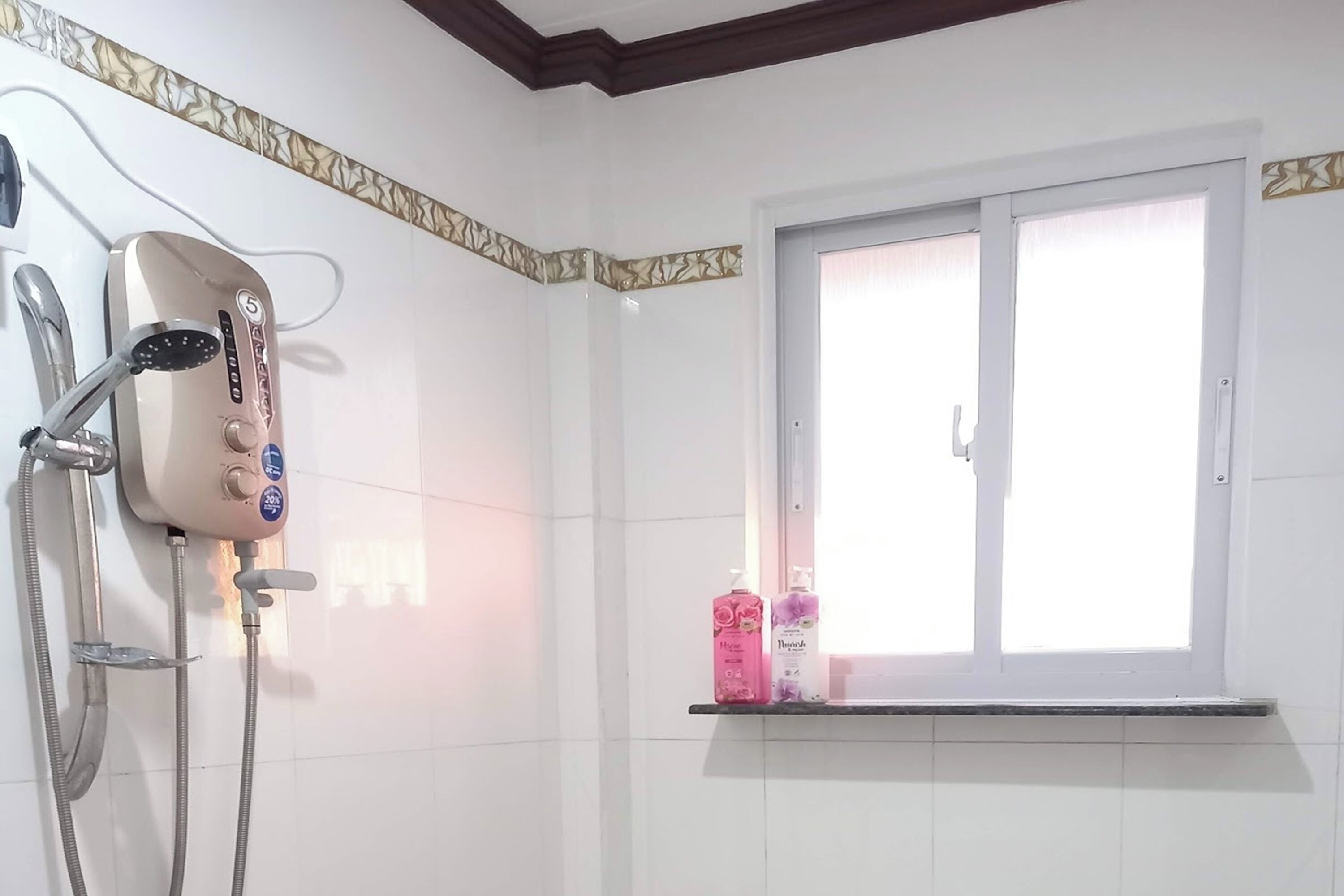 Un baño con ducha, ventana y repisa con artículos de aseo.