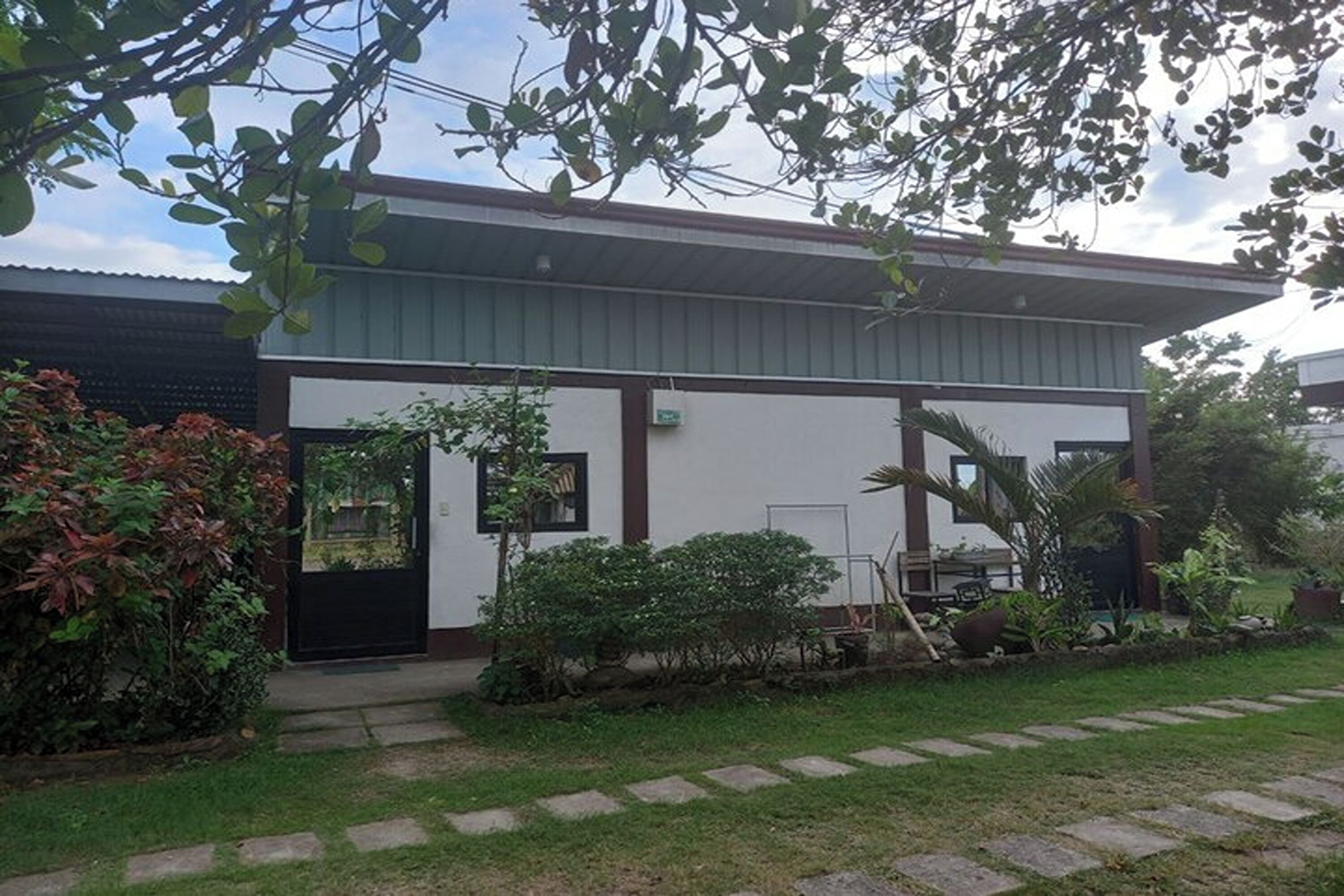 A modern building with a flat roof, a black door, and a small garden area with stepping stones leading to the entrance.