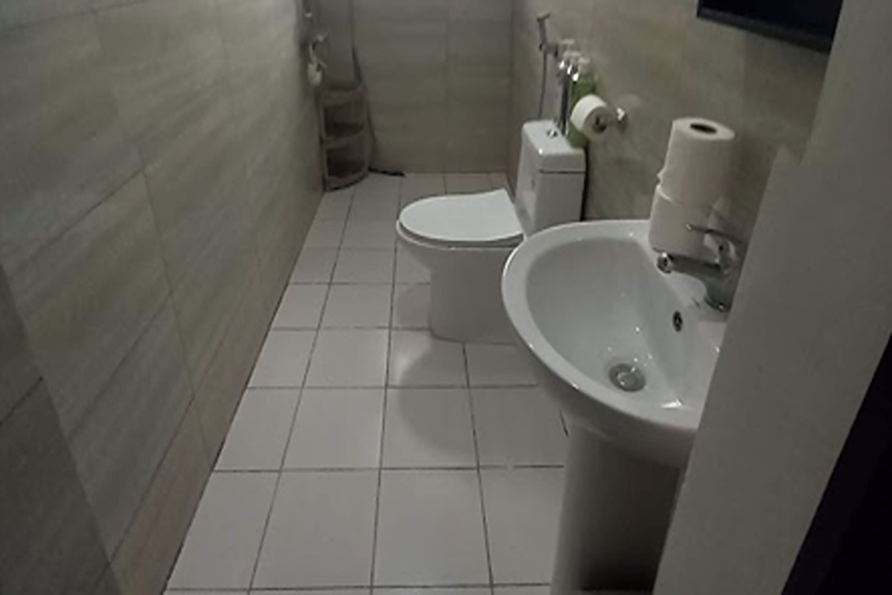A small, tiled bathroom with a toilet, sink, and shower.