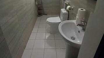 A small, tiled bathroom with a toilet, sink, and shower.
