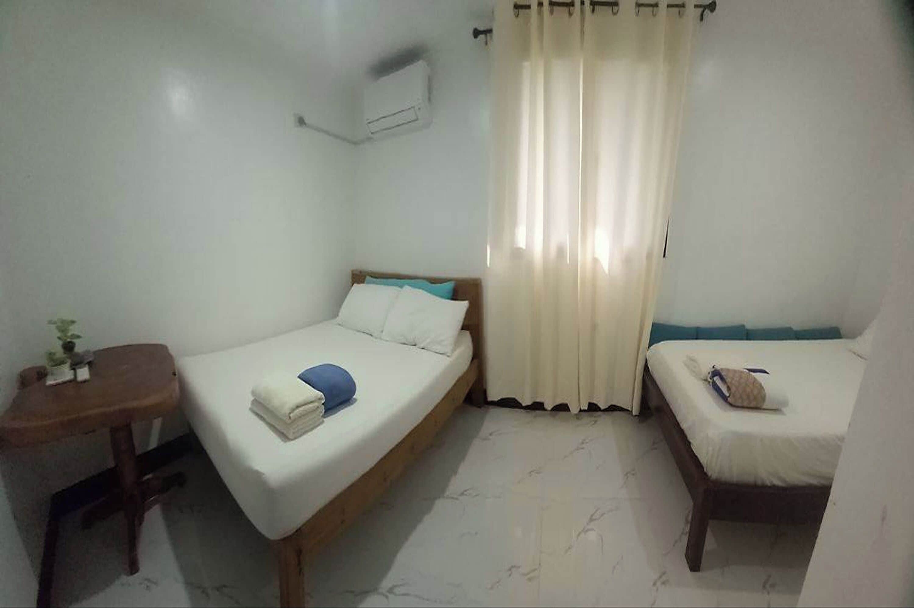 Una habitación pequeña y sencilla con dos camas individuales, una mesita y un aire acondicionado instalado en la pared.