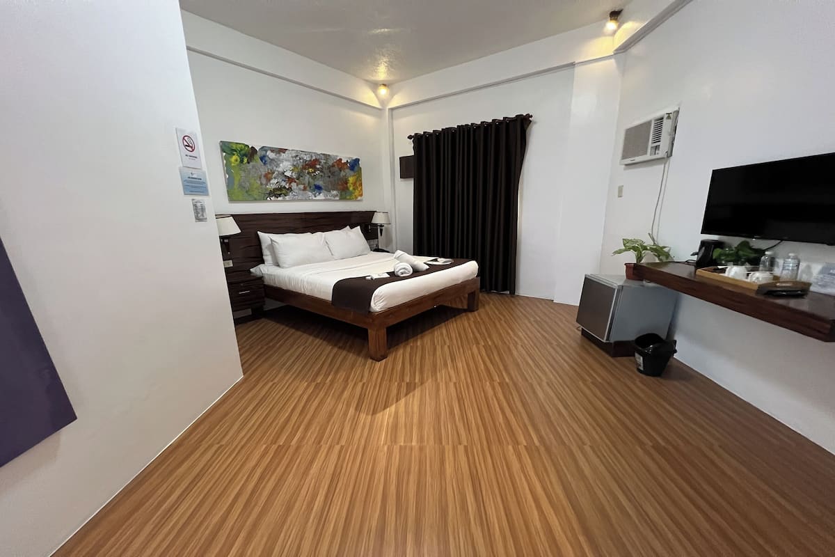 A hotel room with a bed, a desk, a television, and a painting on the wall.