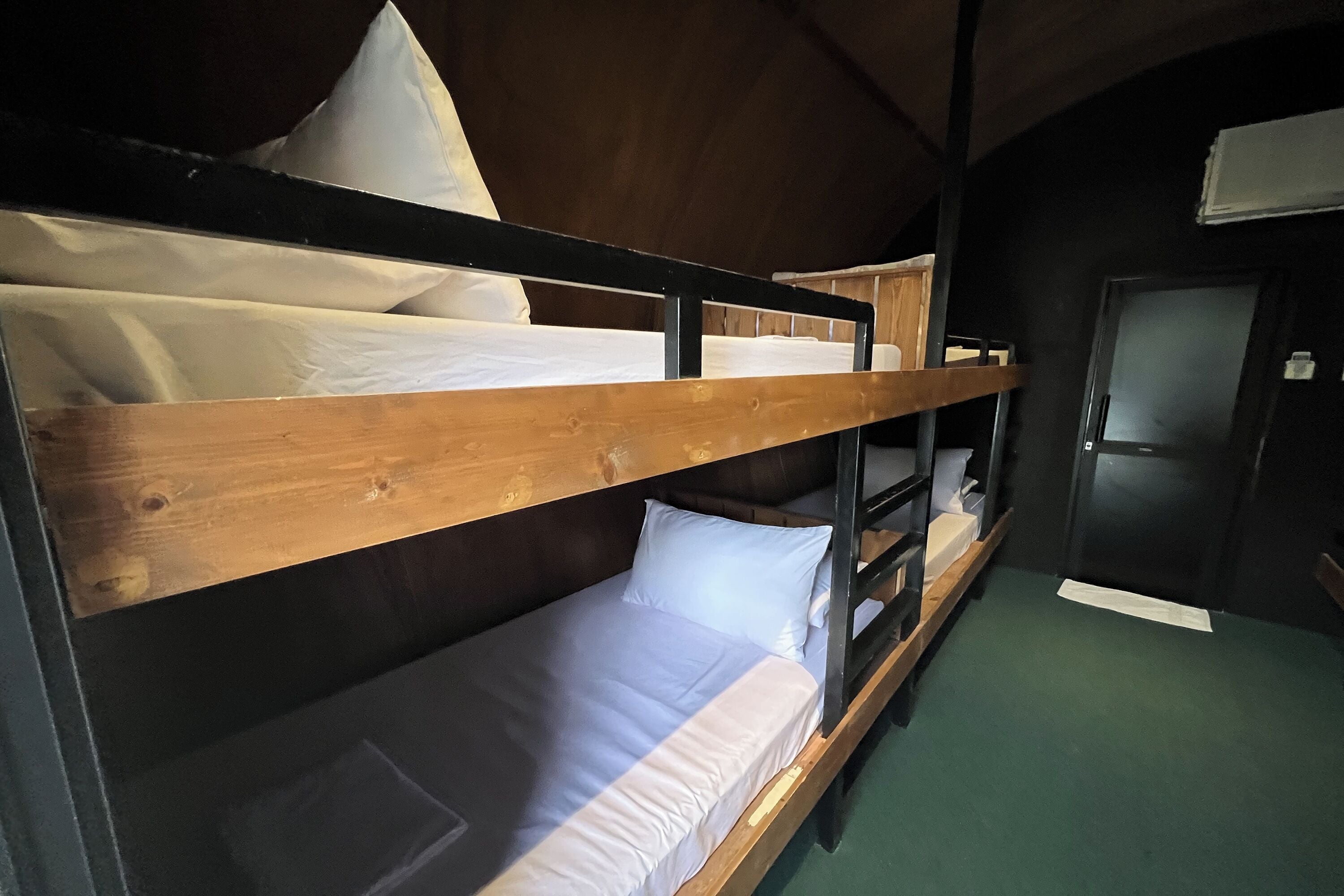 Ein Schlafraum mit Etagenbett aus Holz, einem grünen Teppich und einer Tür.