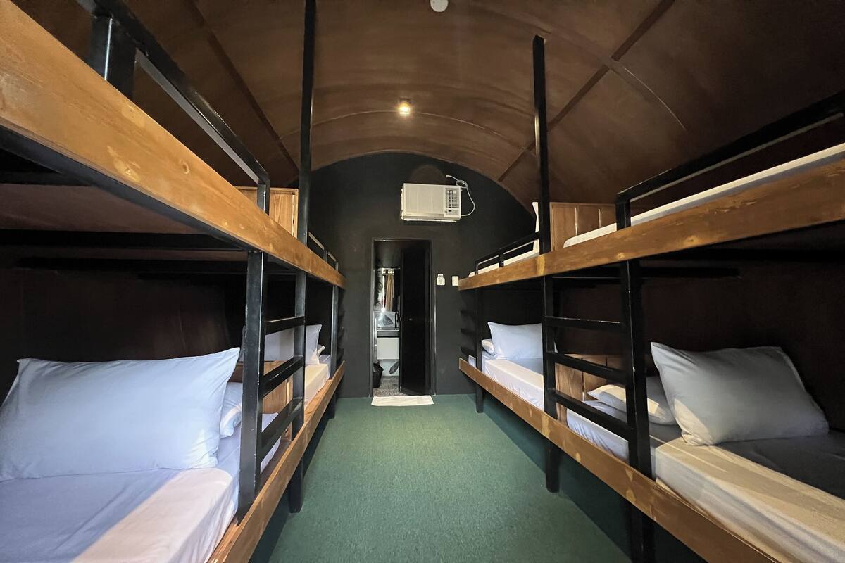 A bunk room with wooden bunk beds, a green carpet, and a ceiling-mounted air conditioning unit.