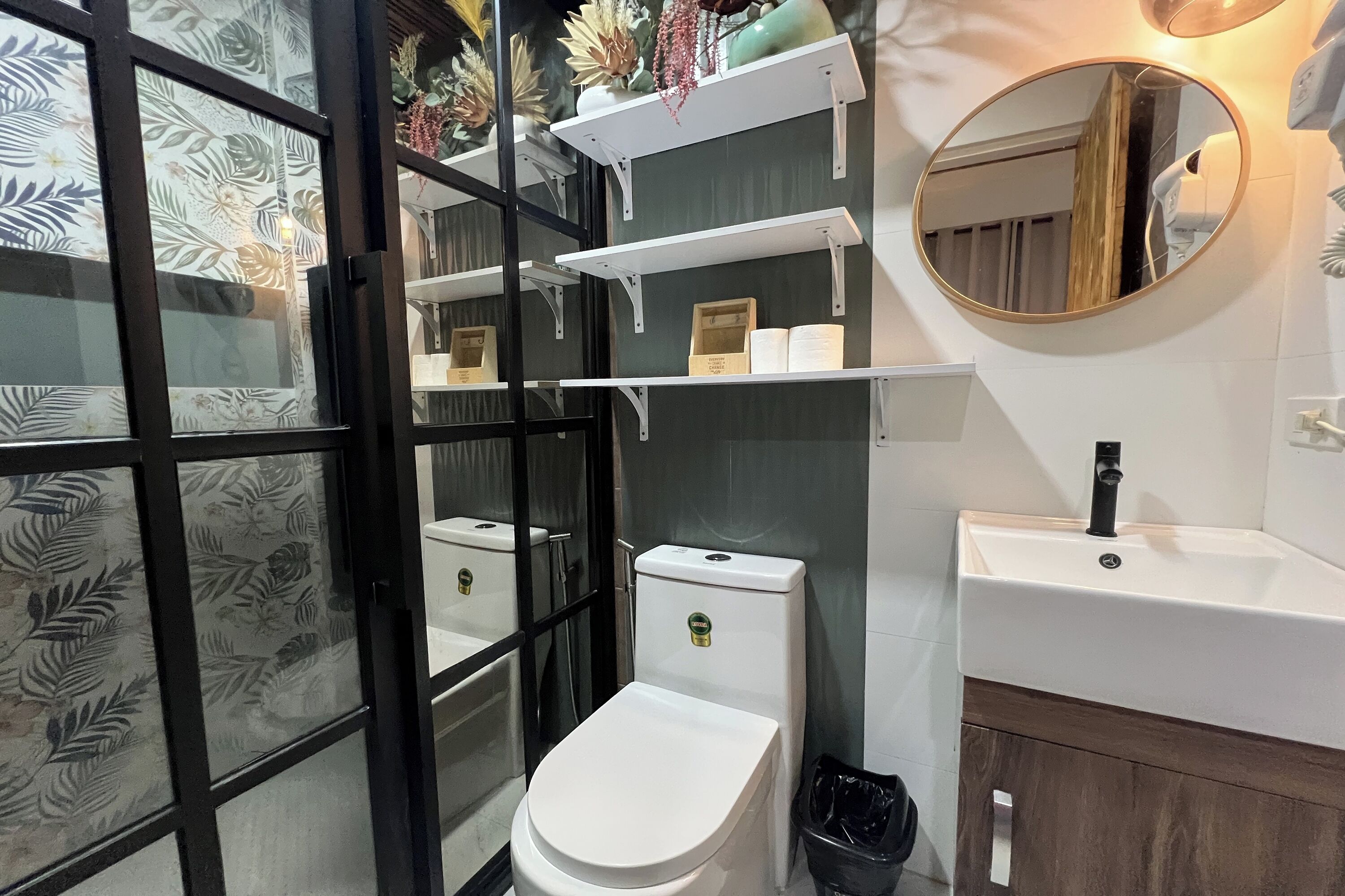 A bathroom with a toilet, a sink, and shelves with toiletries.