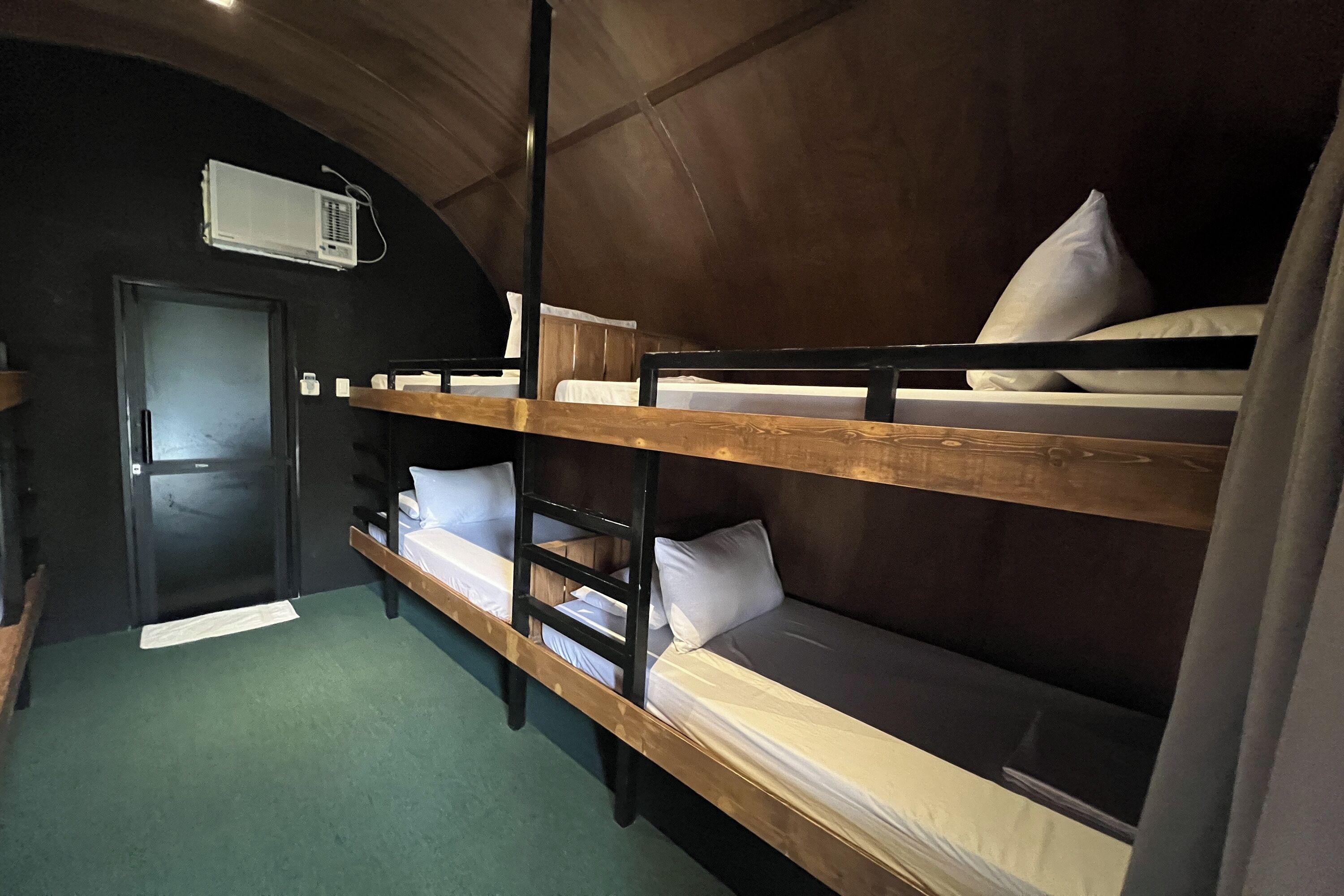 A bunk room with two bunk beds, a wooden ceiling, and a door.
