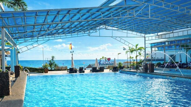 Una piscina con sillas de descanso, una zona cubierta y vista al océano.