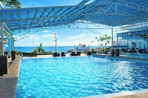 A swimming pool with lounge chairs, a covered area, and a view of the ocean. - Funtasea Hotel and Beach Resort (Iba)