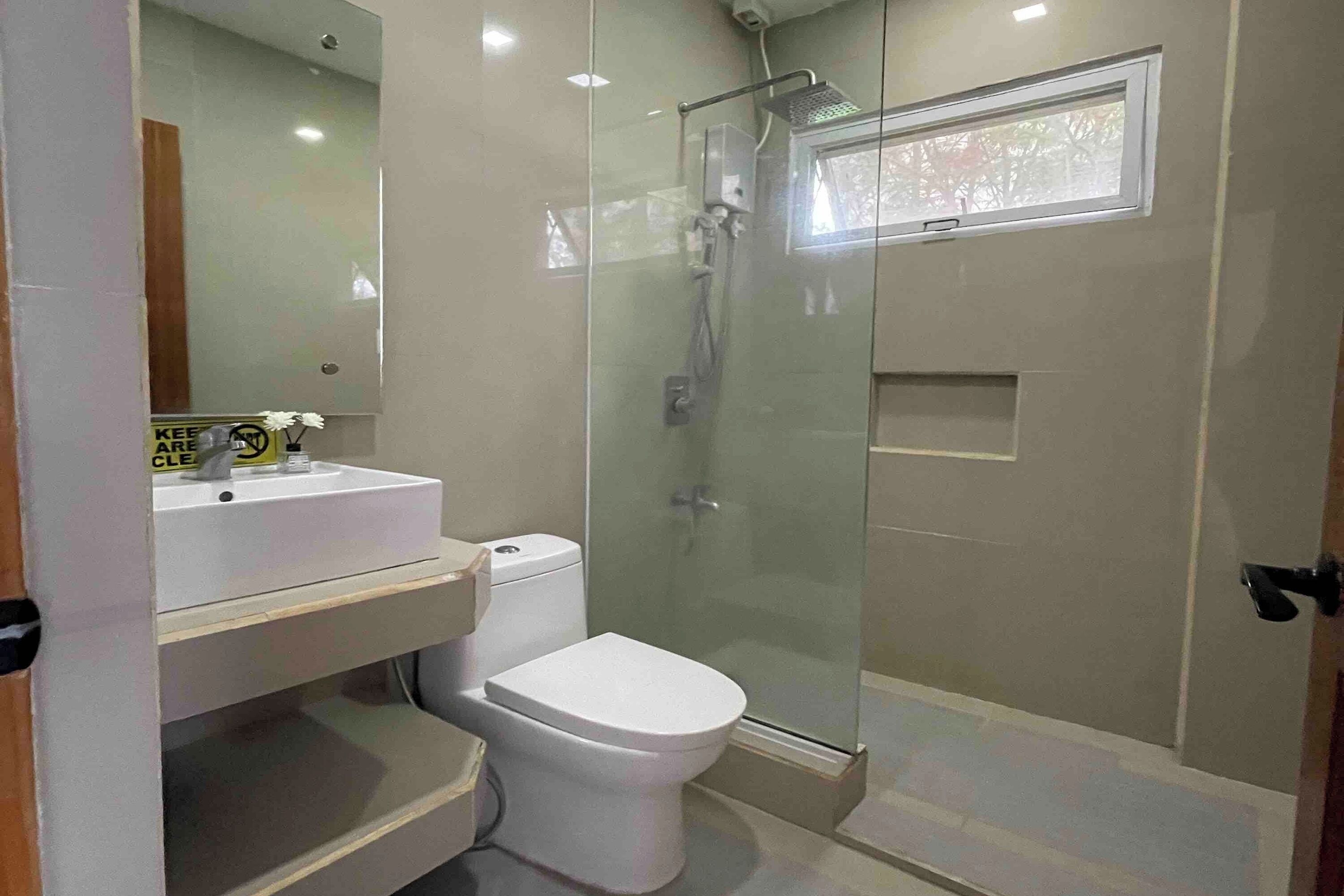 A modern bathroom with a glass-enclosed shower, a white toilet, and a sink with a mirror above it.