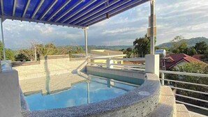 Ein Pool mit blauer Dachkonstruktion, umgeben von einer Steinmauer und mit Blick auf eine hügelige Landschaft.