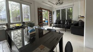 Ein geräumiger Wohnbereich mit Esstisch, schwarzem Ledersofa und großen Fenstern, die einen Blick ins Freie ermöglichen.