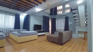Ein modernes Hotelzimmer mit Holzboden, einer Couch, zwei Betten, einem Fernseher und einer Treppe.