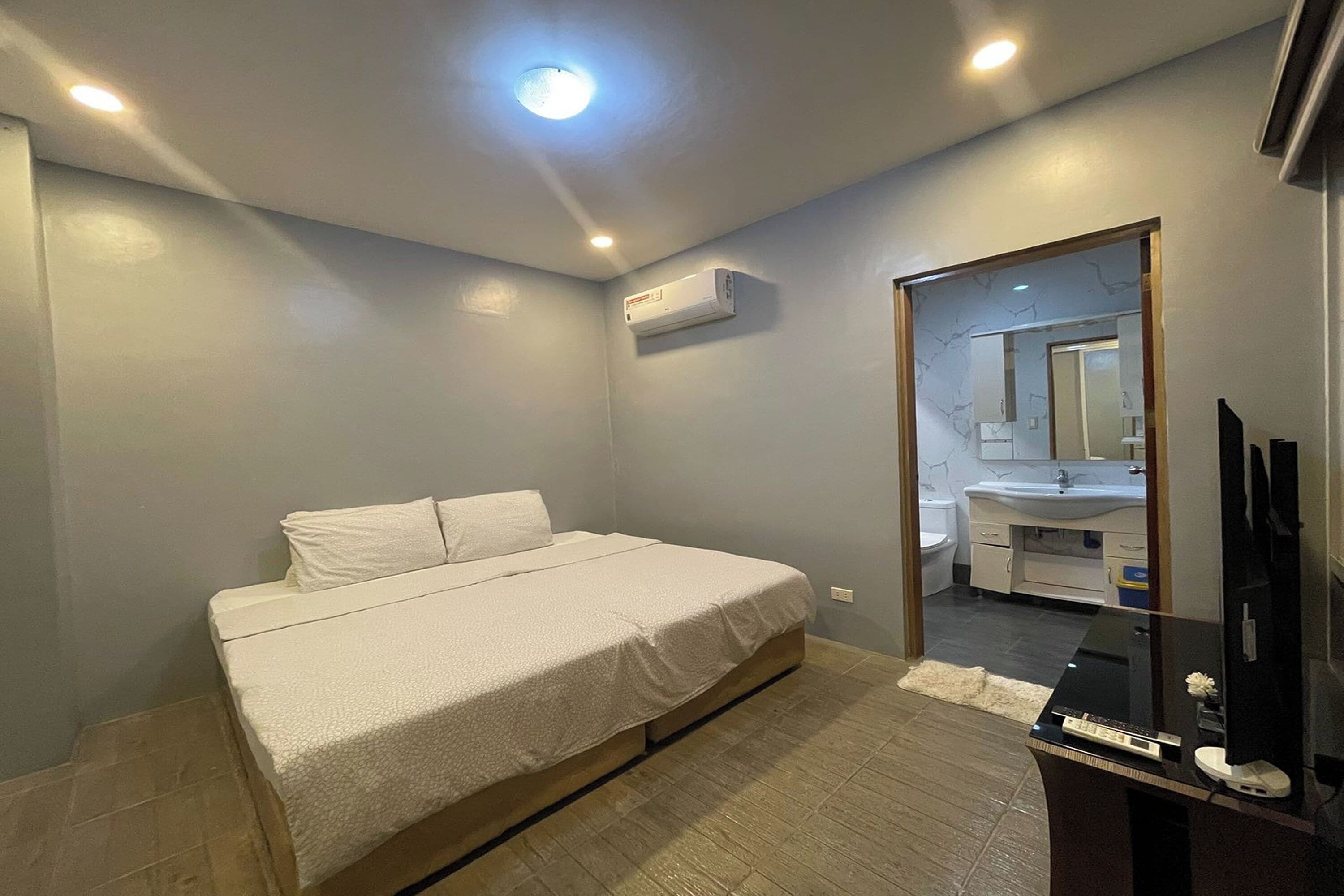 A bedroom with a bed, a TV, and a bathroom visible through a glass door.