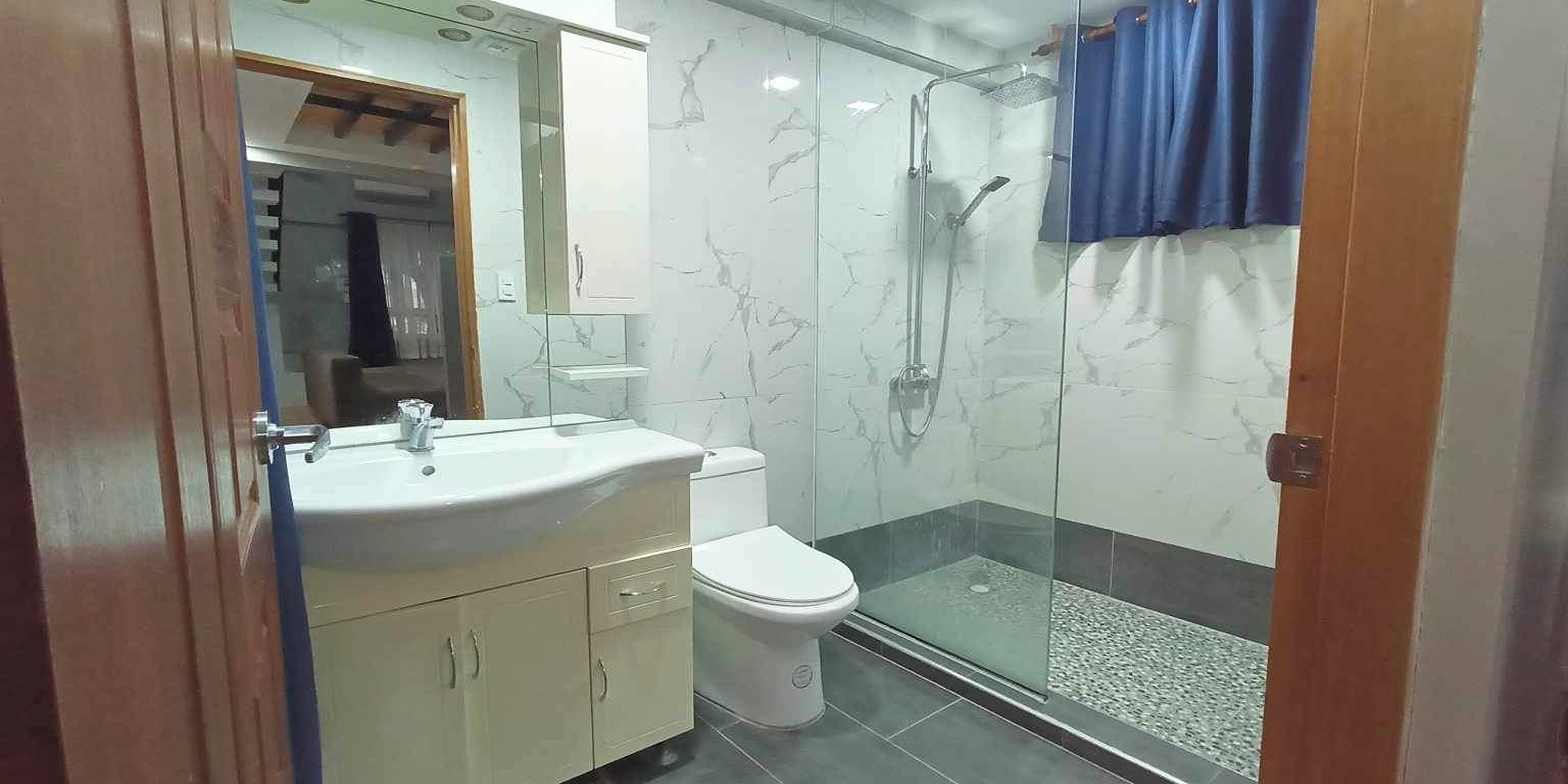Un baño con ducha de vidrio, lavamanos blanco y retrete.