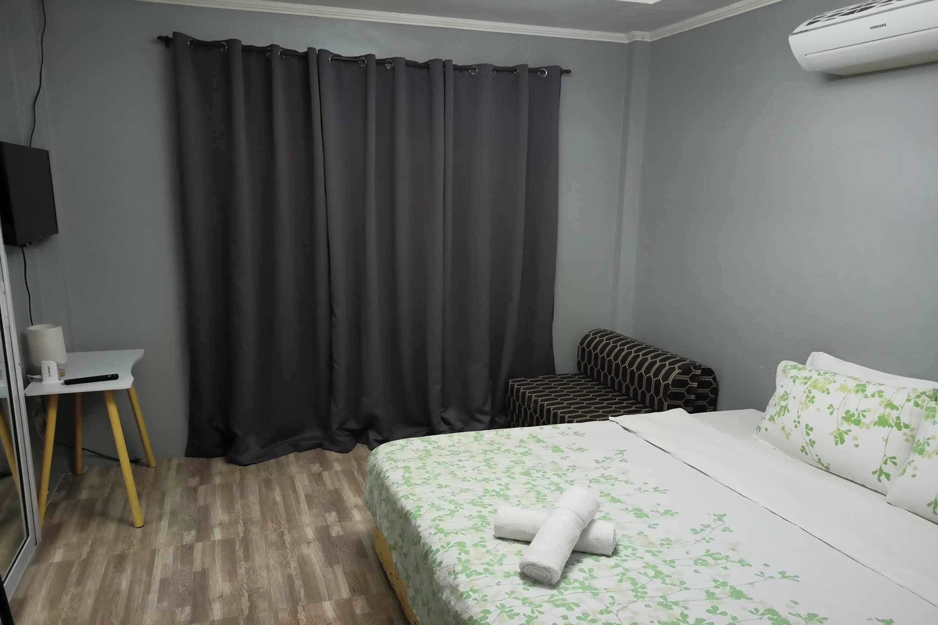 A bedroom with a bed, a small desk, a chair, and a curtain.