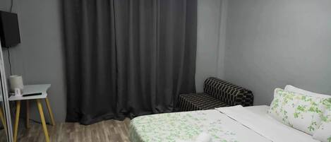 A bedroom with a bed, a small desk, a chair, and a curtain.