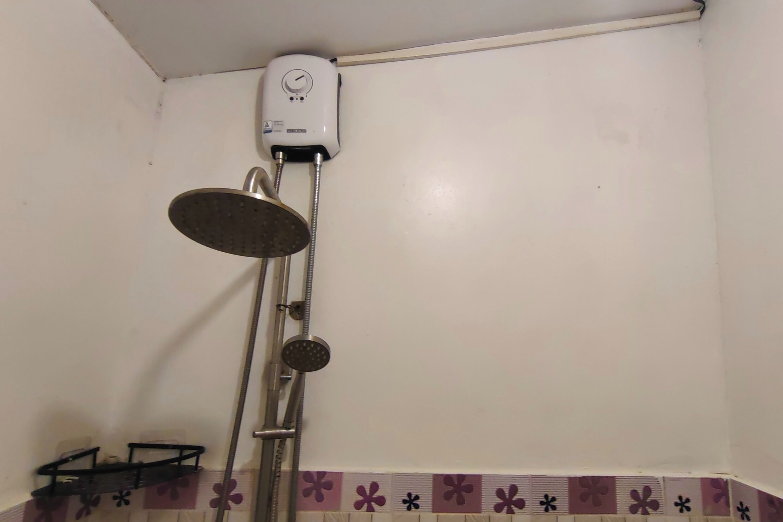 A bathroom with a shower, a white wall, and a shelf with toiletries.