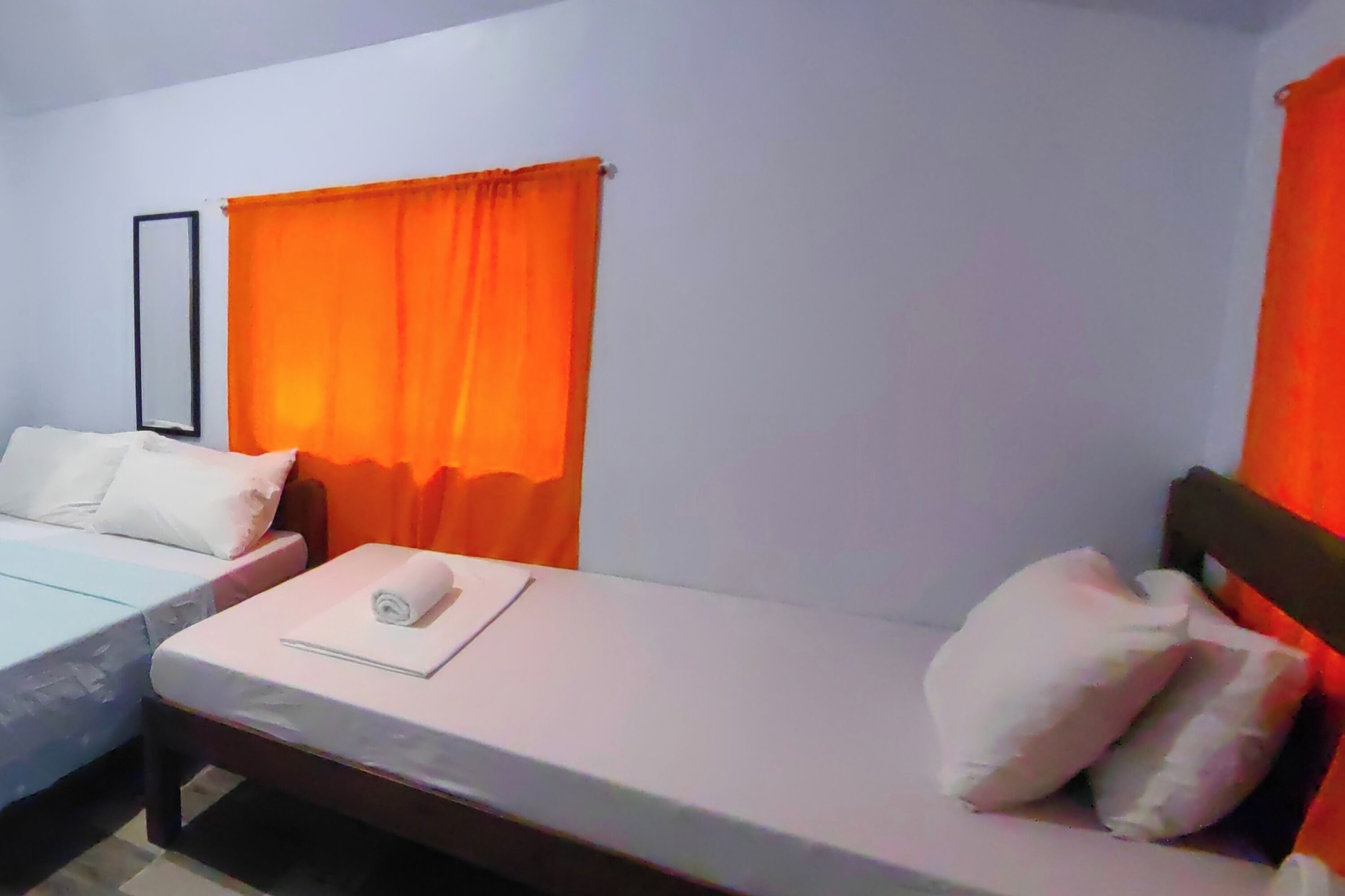 Een hotelkamer met twee eenpersoonsbedden, elk met wit beddengoed en kussens, en een oranje gordijn.