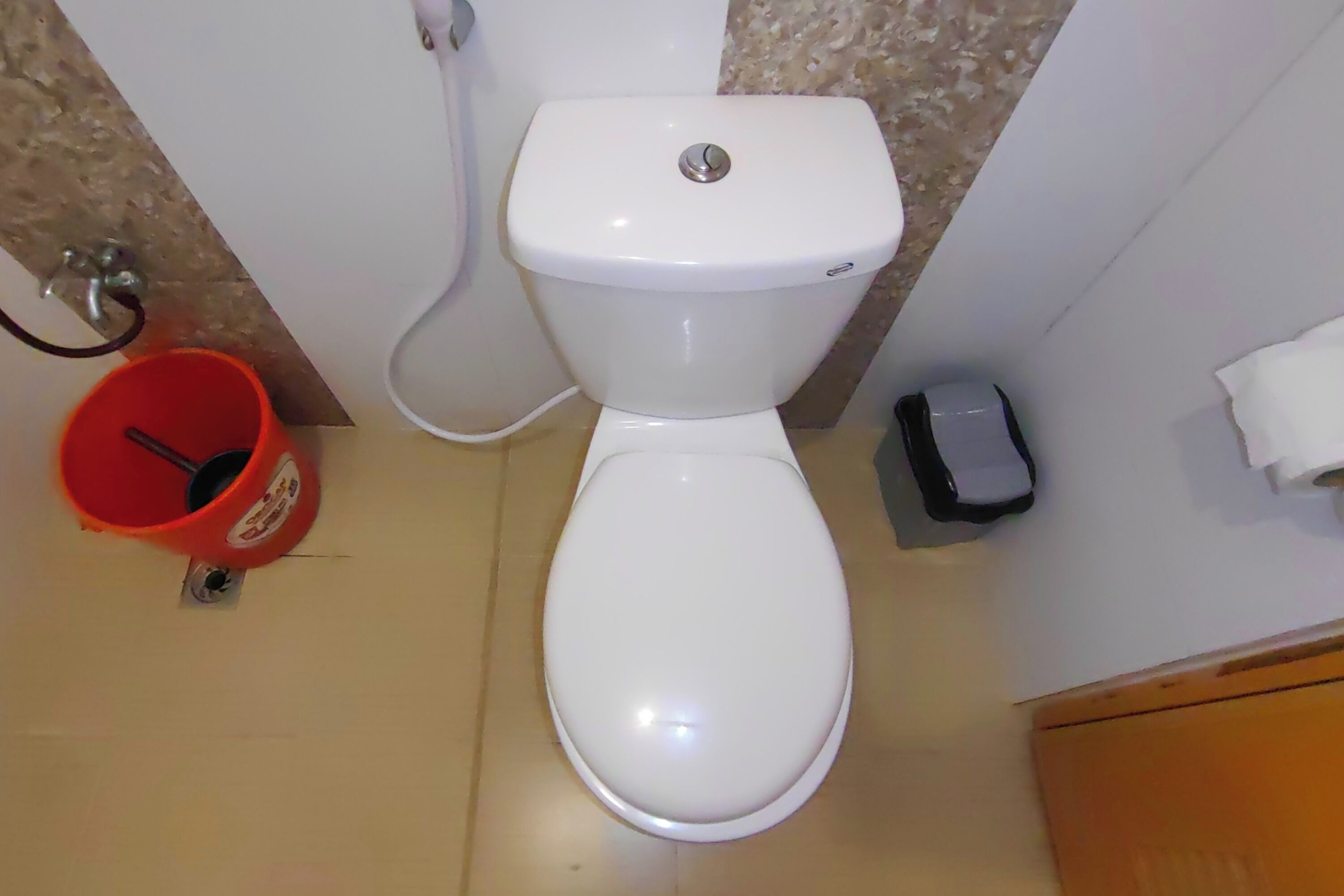 Eine weiße Toilette mit Spülhebel, ein roter Eimer mit schwarzem Tragegriff und ein kleiner Mülleimer.