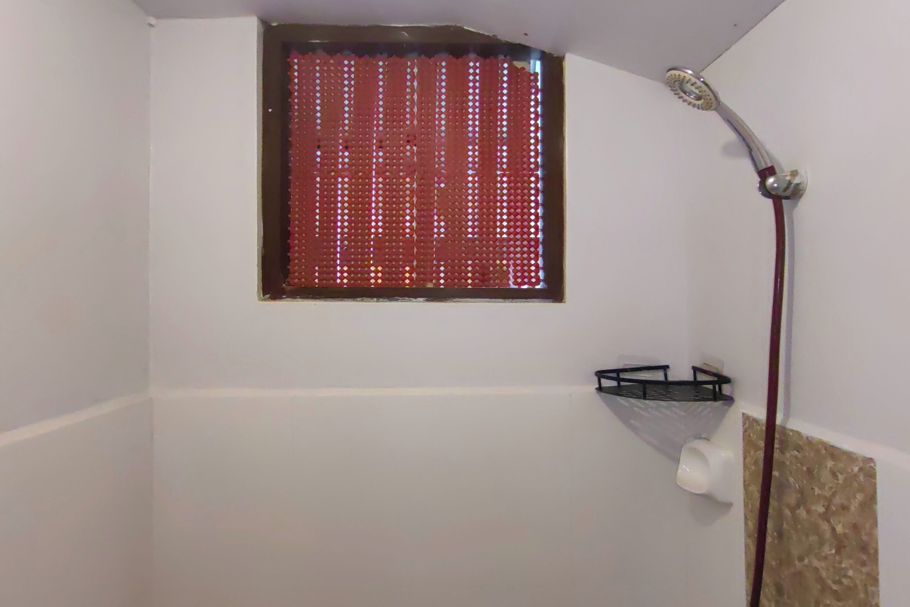 A shower with a red perforated window, a handheld showerhead, and a towel rack.