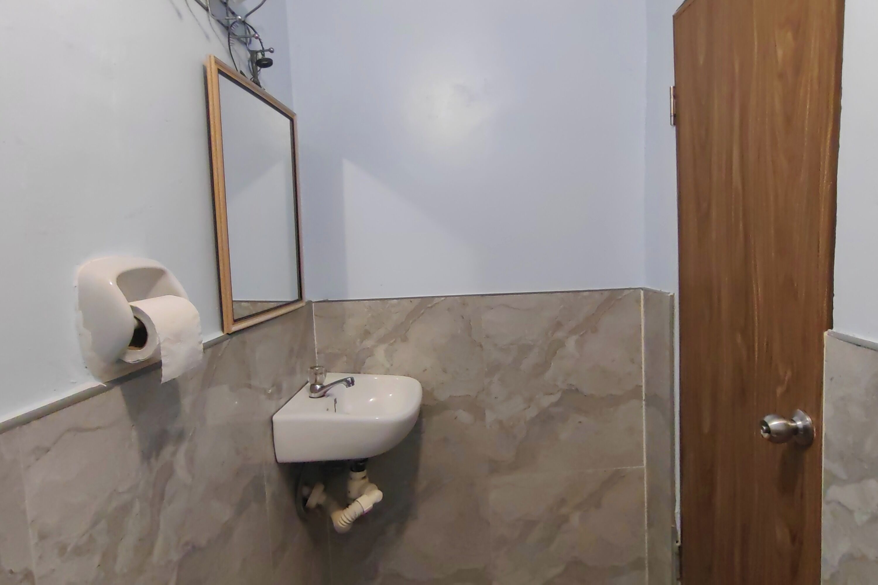 A bathroom with a marble-tiled wall, a white sink, a mirror, and a wooden door.