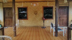 Un espacio exterior techado con piso de madera, dos ventanas y un banco.