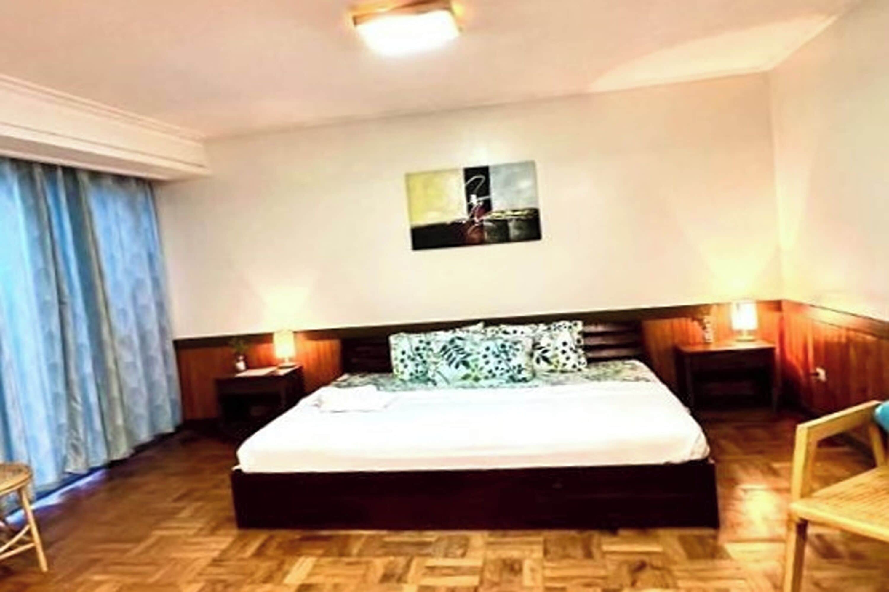 A hotel room with a large bed, two bedside tables, a wall-mounted artwork, and a window with curtains.