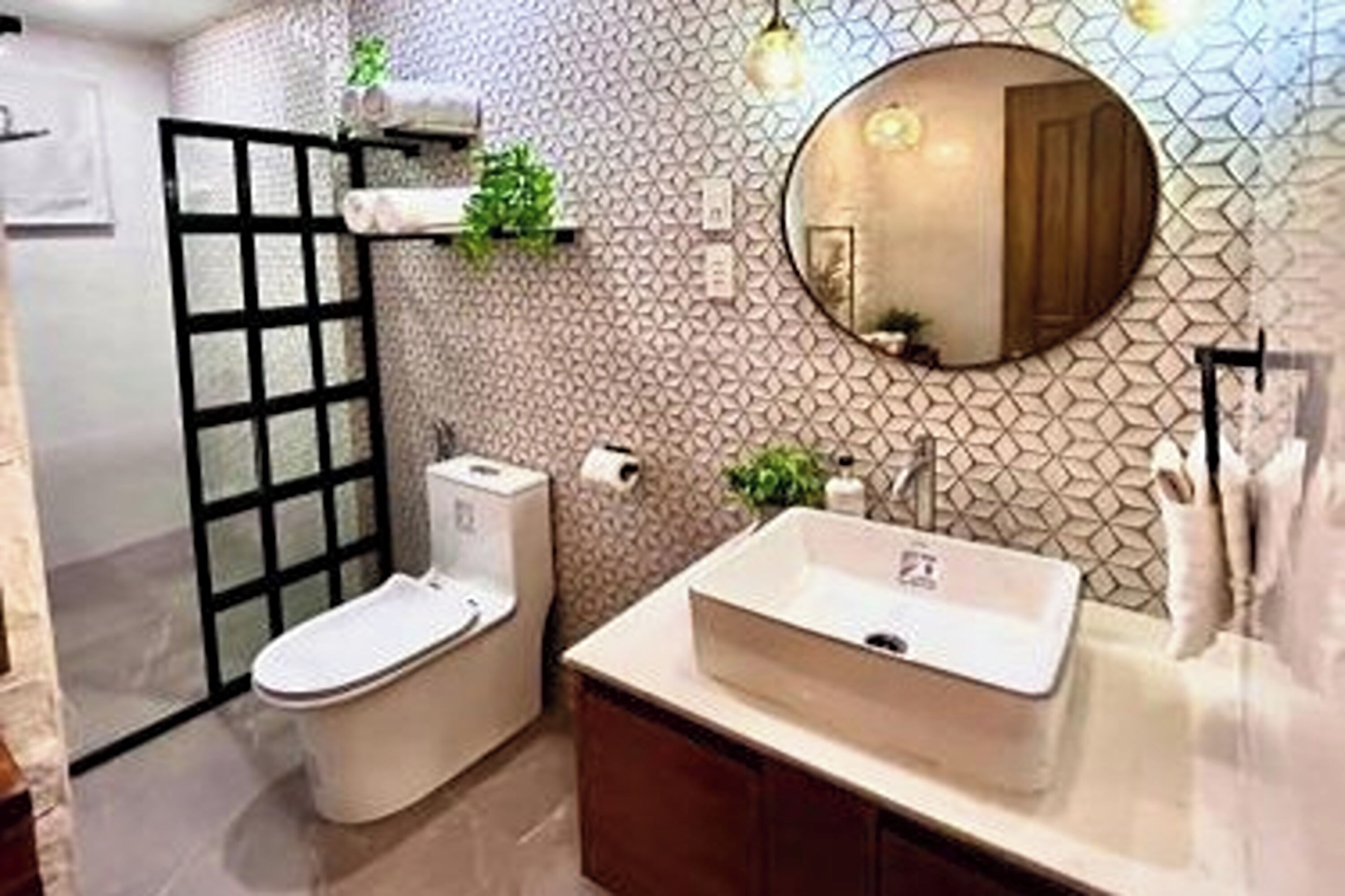 A modern bathroom with a freestanding toilet, a sink with a mirror above it, and a patterned wall.