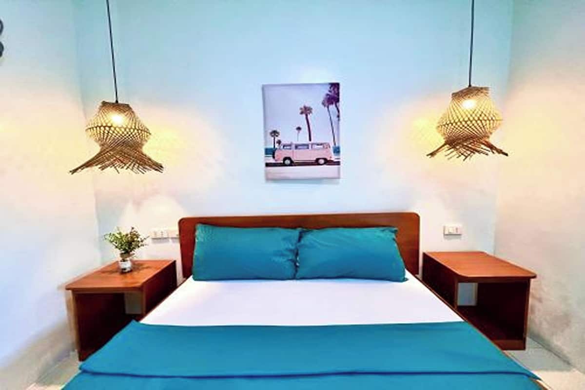 A bedroom with a bed, two nightstands, a wall-mounted picture, and two hanging lamps.