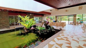 Amplio espacio interior con un estanque de carpas, plantas en macetas y una zona de estar con sillas y mesas.