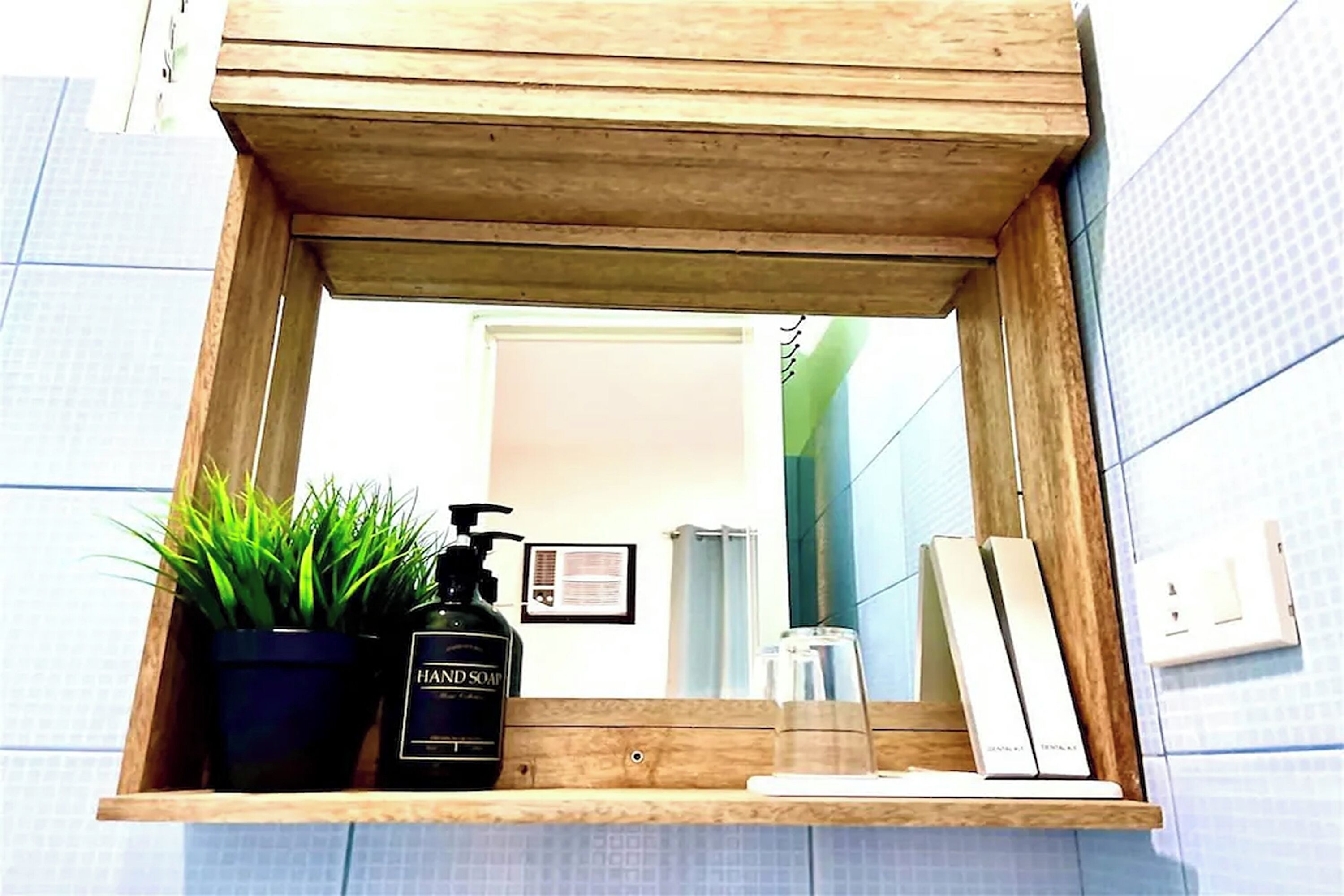 Une étagère en bois avec une plante en pot, un flacon de savon liquide et un verre d’eau.