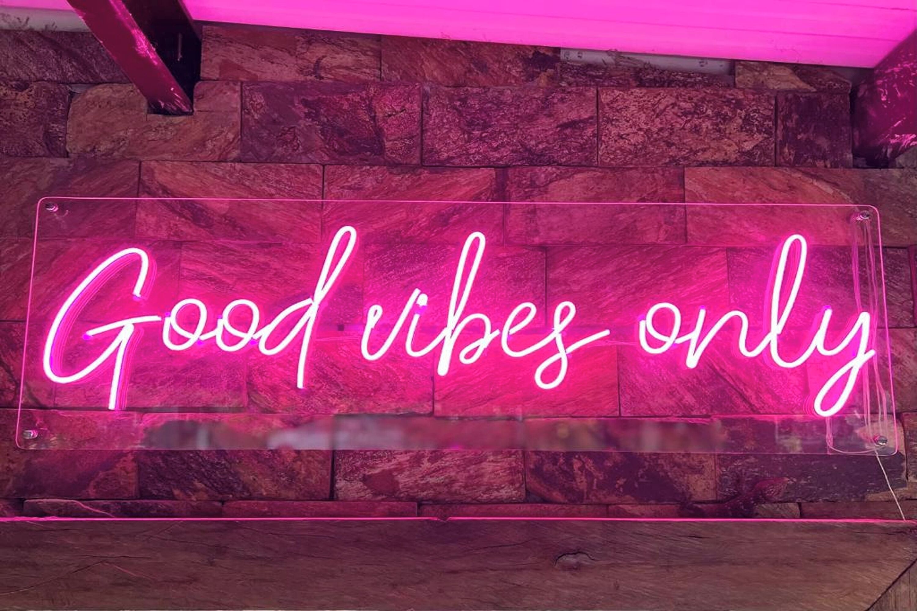 A neon sign with the text "Good vibes only" against a stone wall backdrop.